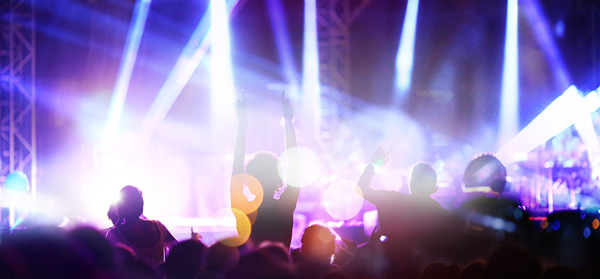 A rock concert from the perspective of someone in the crowd with a stage and lights in the background.